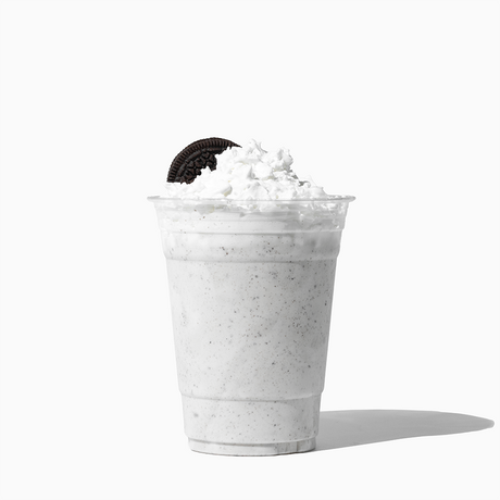 UNIQ 16 oz clear PET plastic cup featuring a cookies and cream milkshake topped with whipped cream and a chocolate sandwich cookie, showcasing premium beverage presentation for wholesale cafes.