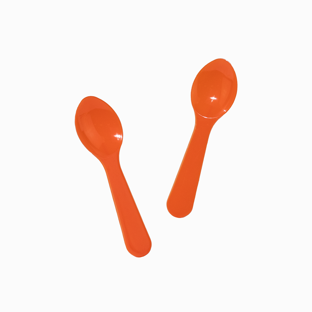 Orange disposable tasting spoons in motion for portioning sweet frozen treats.